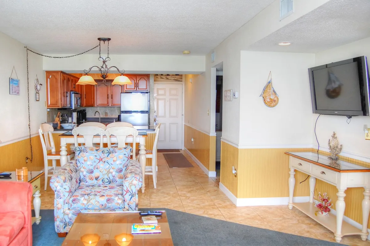 A cozy, welcoming interior with a colorful armchair, a dining table ready for gatherings, a stylish kitchen area, and a television. The scene suggests comfort and relaxation after a day of resort adventures.