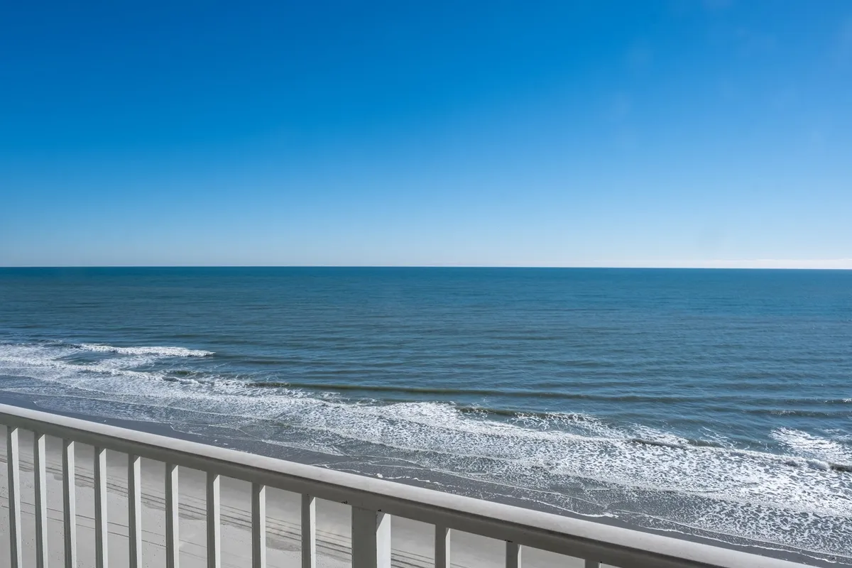 A sweeping view of the ocean, with gentle waves meeting the shore beneath a wide, open sky. The scenery is tranquil, offering a sense of relaxation and tying the resort's location to its coastal backdrop.