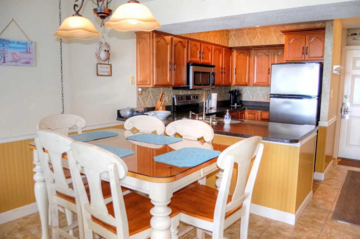 A view of the dining table adjacent to kitchen cabinets and appliances illustrates a seamless flow between the kitchen and social areas. The arrangement encourages communal meals and easy movement between prepping, cooking, and gathering.