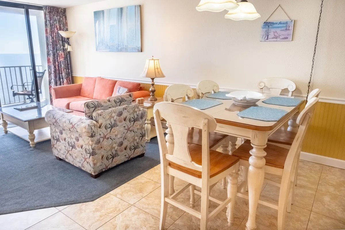 A cozy living area with a comfortable sofa, dining table, and a view of the balcony. The setup is ideal for relaxation or gathering, with soft lighting and a welcoming atmosphere.